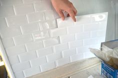 a person is placing white tiles on the wall