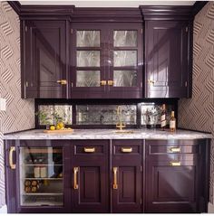 a kitchen with dark wood cabinets and marble counter tops, gold pulls on the doors