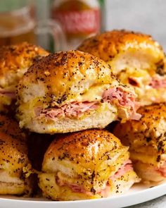 ham and cheese sliders piled on top of each other in a white plate next to a bottle of beer