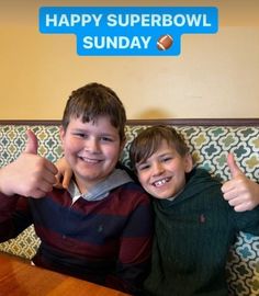 two young boys giving thumbs up in front of a sign that says happy superb bowl sunday