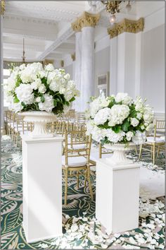 two vases filled with white flowers sit on pedestals in the middle of a room