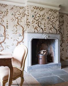 a room with a fireplace, chairs and a wallpapered wall in the background