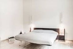 a white bed sitting in the middle of a bedroom next to a wall mounted lamp