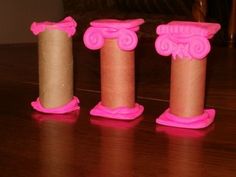 three pink candles sitting on top of a wooden table next to two rolls of toilet paper