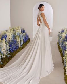 a woman standing in front of flowers wearing a white wedding dress with open back and train