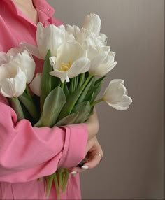 a woman holding a bouquet of white tulips in her hands and wearing a pink shirt