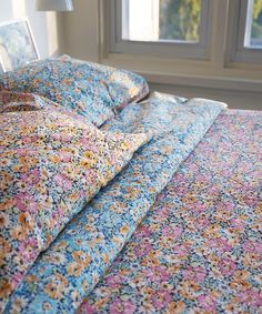 an unmade bed with blue and pink floral bedspread in front of a window