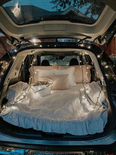 the back end of a car with its trunk open and pillows on it's bed