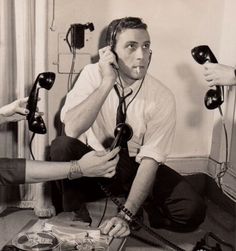 a black and white photo of a man sitting on the floor with two telephones