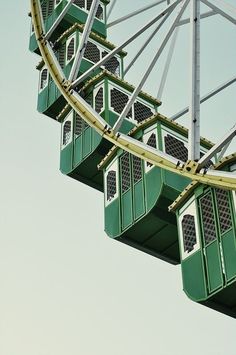 the ferris wheel is green and white with windows on it's sides that allow people to ride