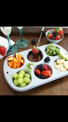 a tray filled with different types of fruit on top of a wooden table next to wine glasses