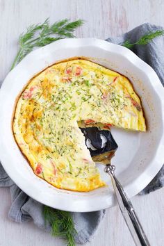 an omelet in a white dish with a piece missing from it and a serving spoon