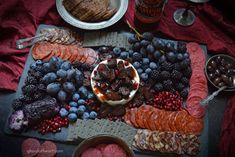 an assortment of meats, fruits and bread on a platter with wine glasses