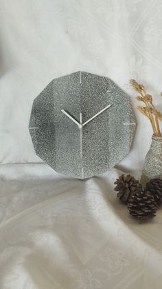 a clock sitting on top of a table next to a vase with pine cones in it