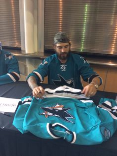 a man sitting at a table with a jersey on it and another person standing next to him