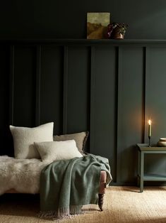 a bedroom with dark green walls and white fur on the bed, next to a small table