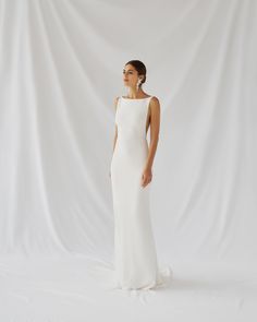 a woman standing in front of a white backdrop wearing a wedding dress with an open back