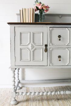 an old white cabinet with some books on top and flowers in the vase next to it