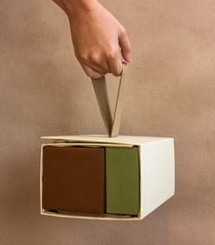 a hand holding a knife over a box with two different colored boxes on it's sides