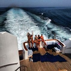 four women in bikinis are sitting on the back of a boat with their arms up