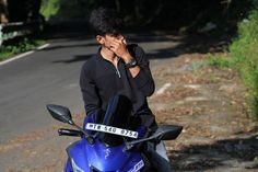 a man standing next to a blue motorcycle on the side of a road with trees in the background