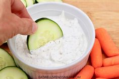 cucumber dip in a white bowl surrounded by carrots and celery