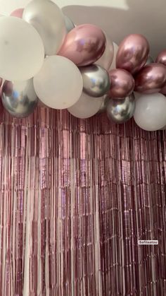 balloons and streamers are hanging from the ceiling in front of a pink curtain with metallic foil