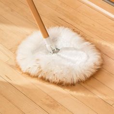 a mop is on top of a fluffy white duster in the middle of a wooden floor