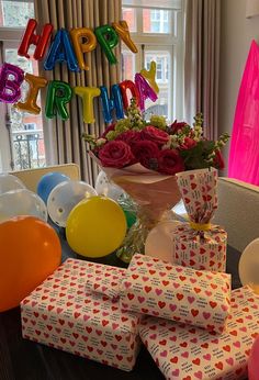 a table topped with lots of presents next to balloons and birthday letters hanging from the ceiling