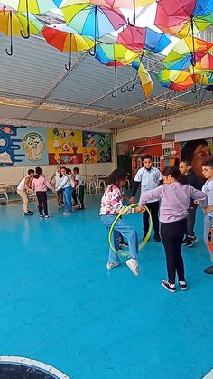 several children are playing with colorful umbrellas in an indoor gym area while others watch