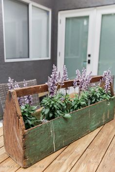 a wooden box filled with purple flowers sitting on top of a wooden table next to a door