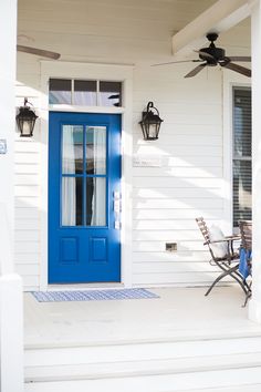 a blue front door on a white house with two chairs and a table in front