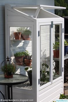 a small white greenhouse with potted plants in it's windows and shelves on the side of a house