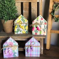 three small houses are sitting next to each other on a wooden bench with potted plants in the background