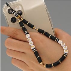 a hand holding a cell phone with a black and white beaded necklace on it