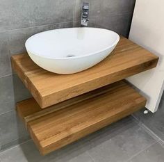 a white bowl sitting on top of a wooden shelf next to a wall mounted faucet