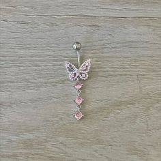 a pink and white butterfly belly ring on a wooden table with wood grained background