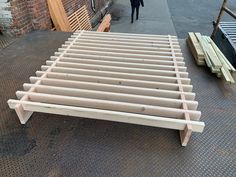 a bed frame sitting on top of a sidewalk next to a building and a person walking by