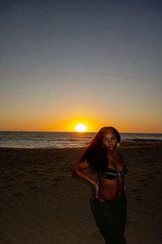 a woman standing on top of a sandy beach next to the ocean at sun set