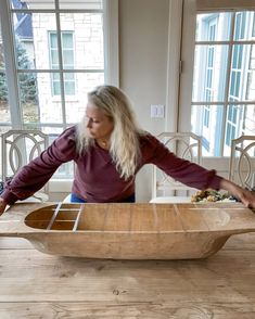 a woman standing in front of a wooden boat on top of a table next to a window