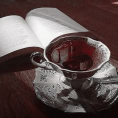 an open book on a wooden table next to a glass cup with liquid in it