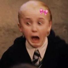 a young boy with a pink bow on his head is making a surprised face while wearing a sweater and tie