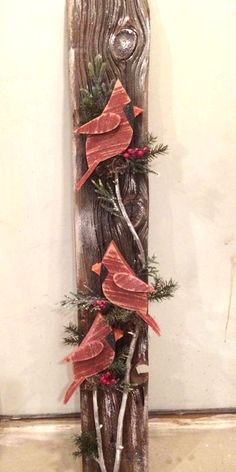 a wooden sculpture with red birds and pine branches on it's sides, in front of a white wall