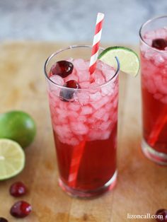 two glasses filled with ice and cranberries on top of a wooden cutting board