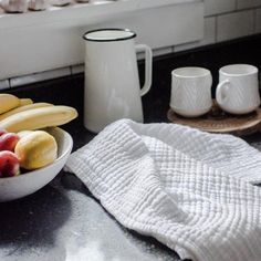 a bowl of fruit sitting on top of a counter next to two cups and a towel