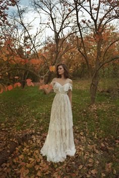 a woman is standing in the leaves with her arms out and wearing a white dress