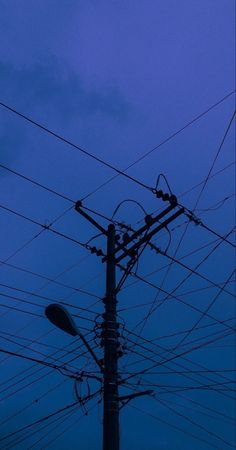 telephone poles and wires against a blue sky at night with the moon in the distance