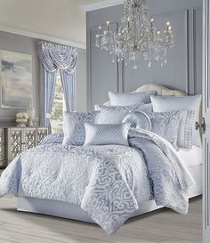 a blue and white comforter set with chandelier in the background on a wooden floor