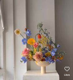 a vase filled with lots of colorful flowers on top of a white table next to a window