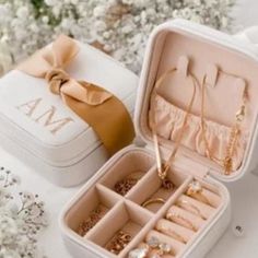 an open white box with jewelry inside sitting on a table next to flowers and greenery